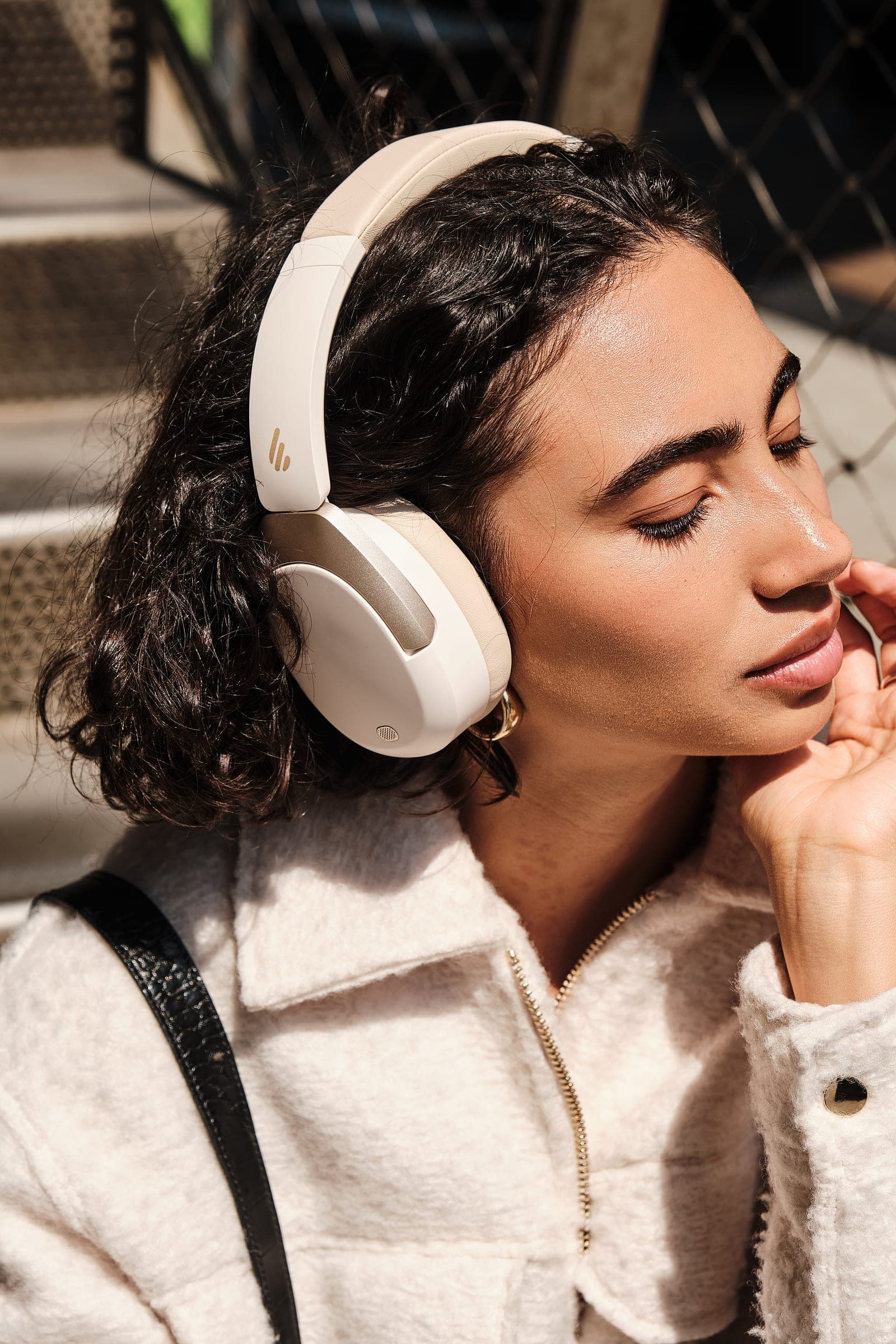 A woman in a cream jacket listening with her eyes closed
